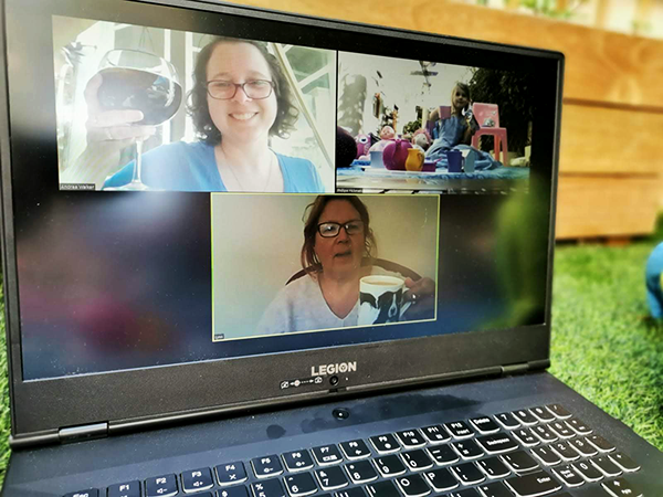 Three people have a video chat together on laptop seated in garden