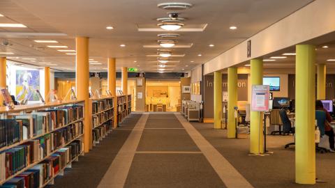 Long passage lined with referencing book shelves to the left. Orange and yellow pillars from floor to ceiling