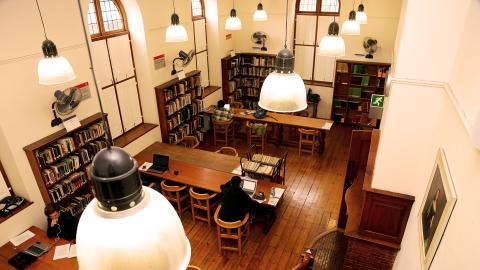 Top view of the Drama Room inside Hiddingh Hall Library. Students seated at long desks with ovehead lighting.