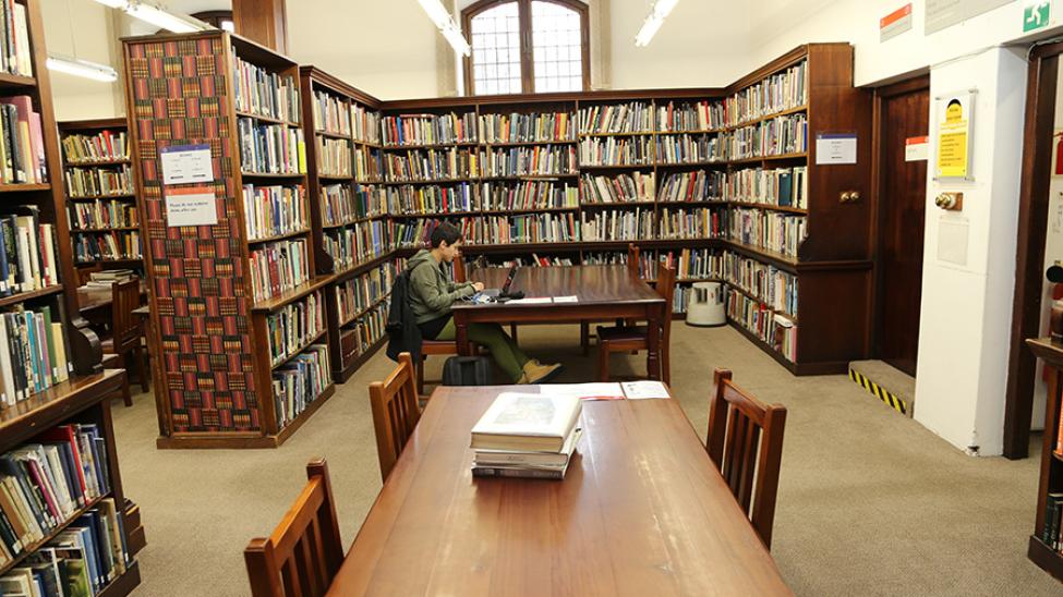 Student seated at table between book stacks in the Hiddingh Hall Library main reading room